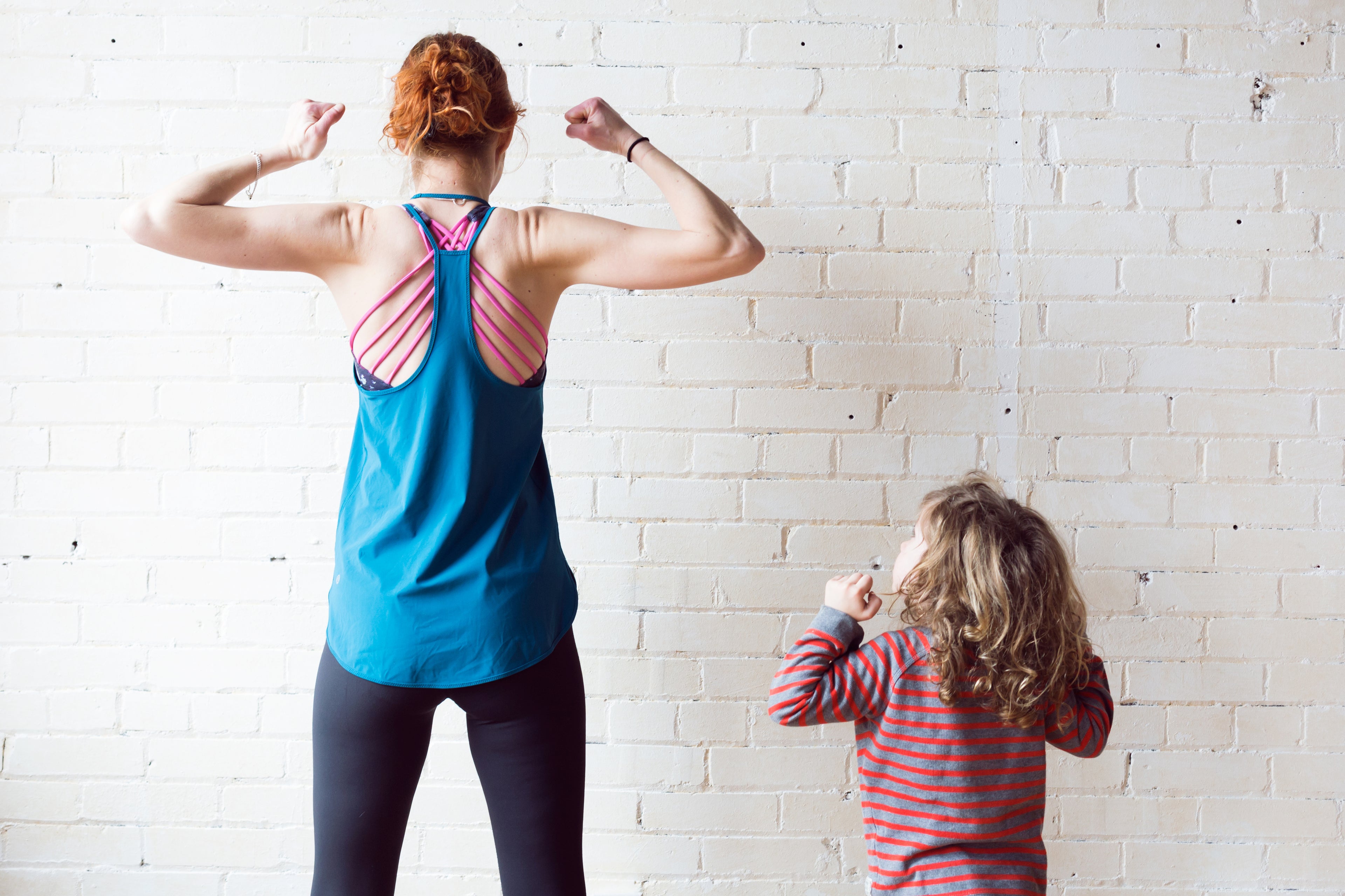 A small child flexing muscles while looking up at their mother